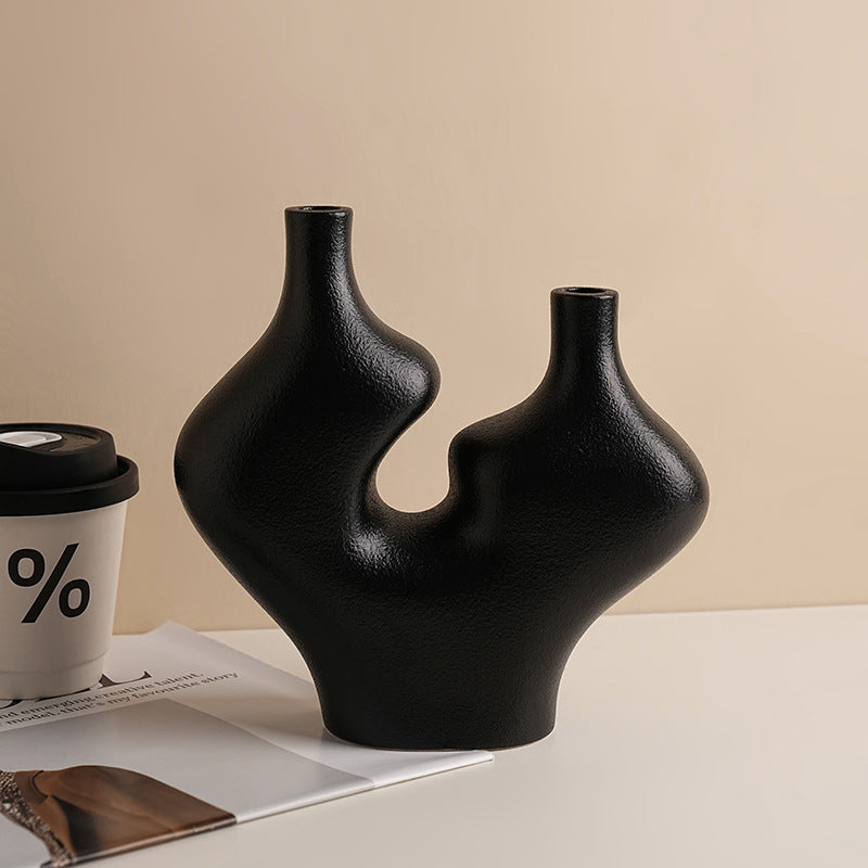 Black abstract vase on a beige surface with a coffee cup and magazine in the background