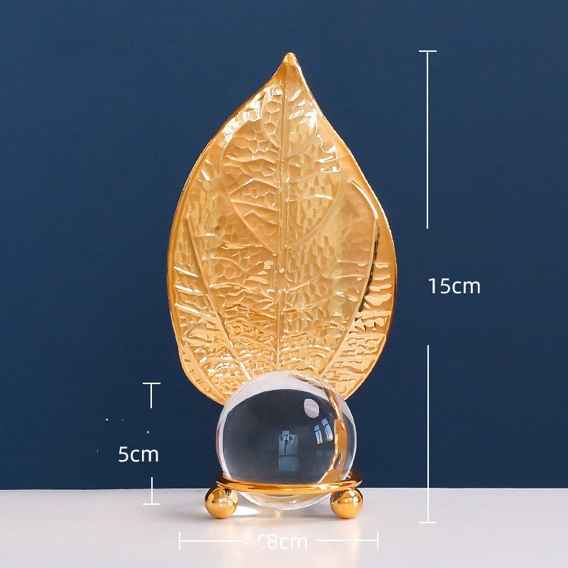 Gold leaf-shaped decorative item with a clear sphere on a blue background
