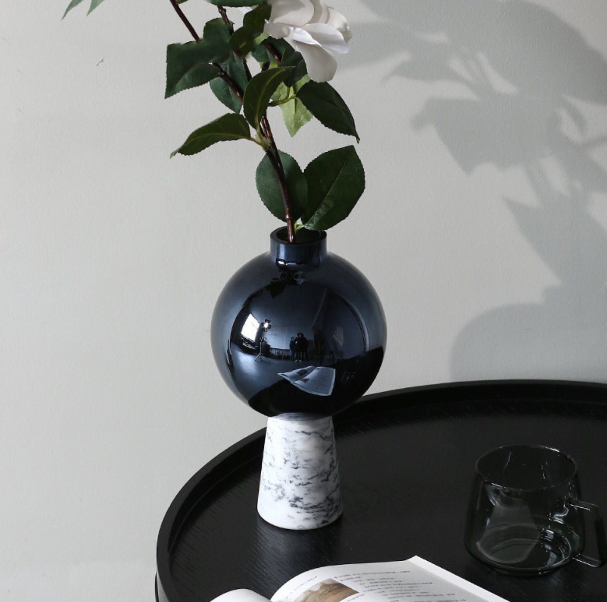 Black vase with a marble base on a dark surface with a light gray background