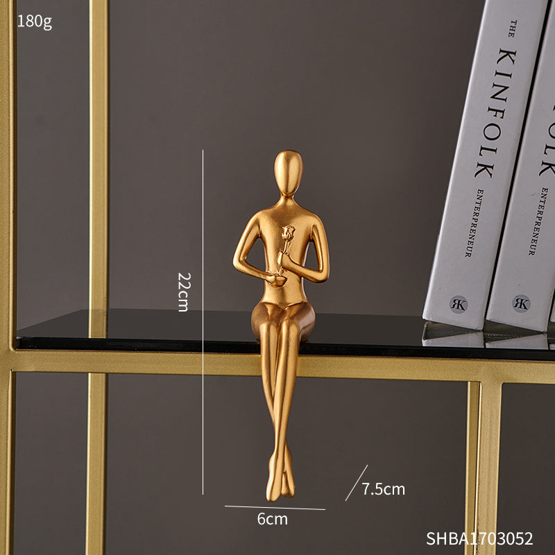 Gold sculpture of a seated figure on a black surface with measurement details.