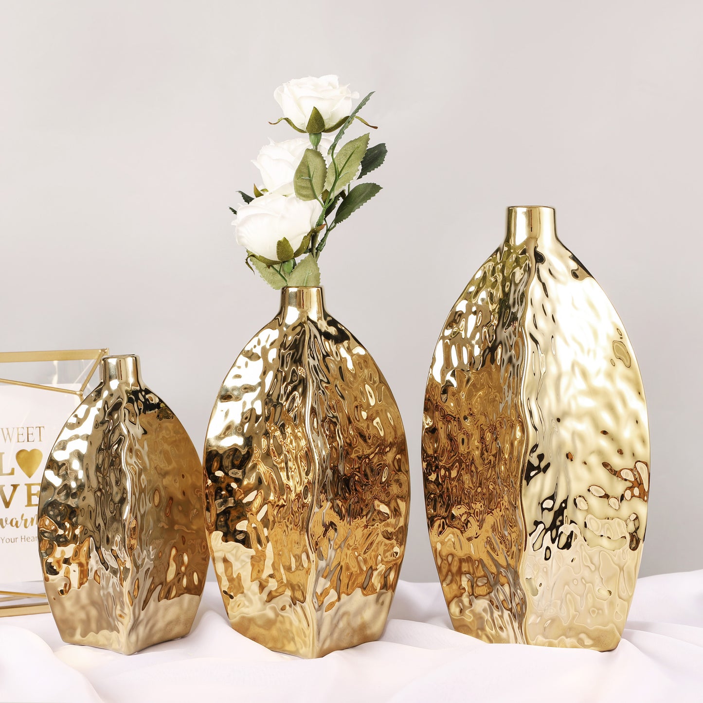 Hammered gold ceramic vase – irregular sculptural shape
Set of three hammered gold vases in S/M/L on table
Modern glam gold ceramic vase with white flowers – DECASA by VS