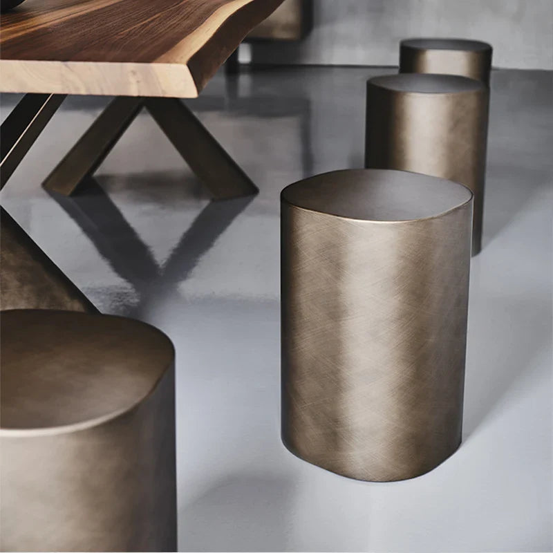 Bronze cylindrical stools on a concrete floor with a wooden table in the background