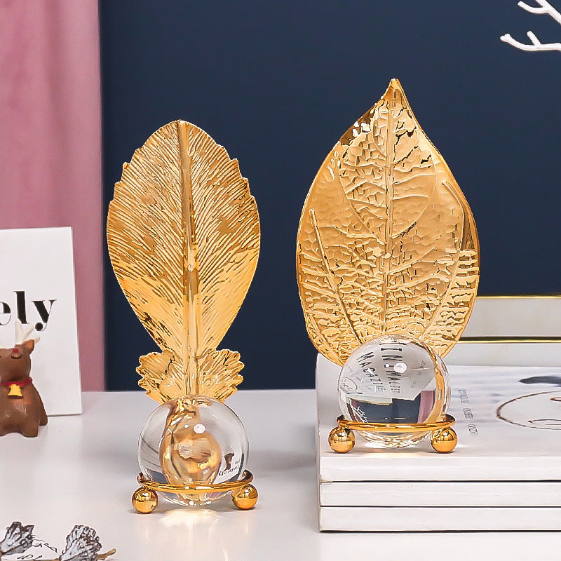 Two gold leaf-shaped decorative items on a surface with a blurred background