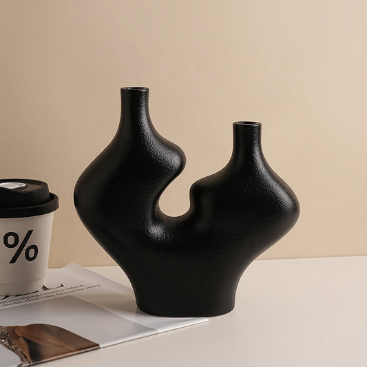 Black abstract vase on a beige surface with a coffee cup and magazine in the background