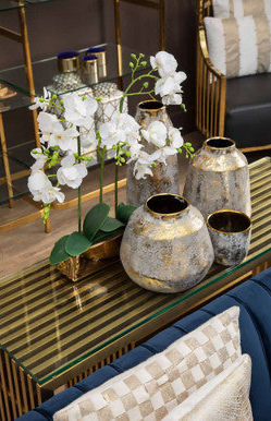 Decorative setup with white flowers in gold and silver vases on a glass table.