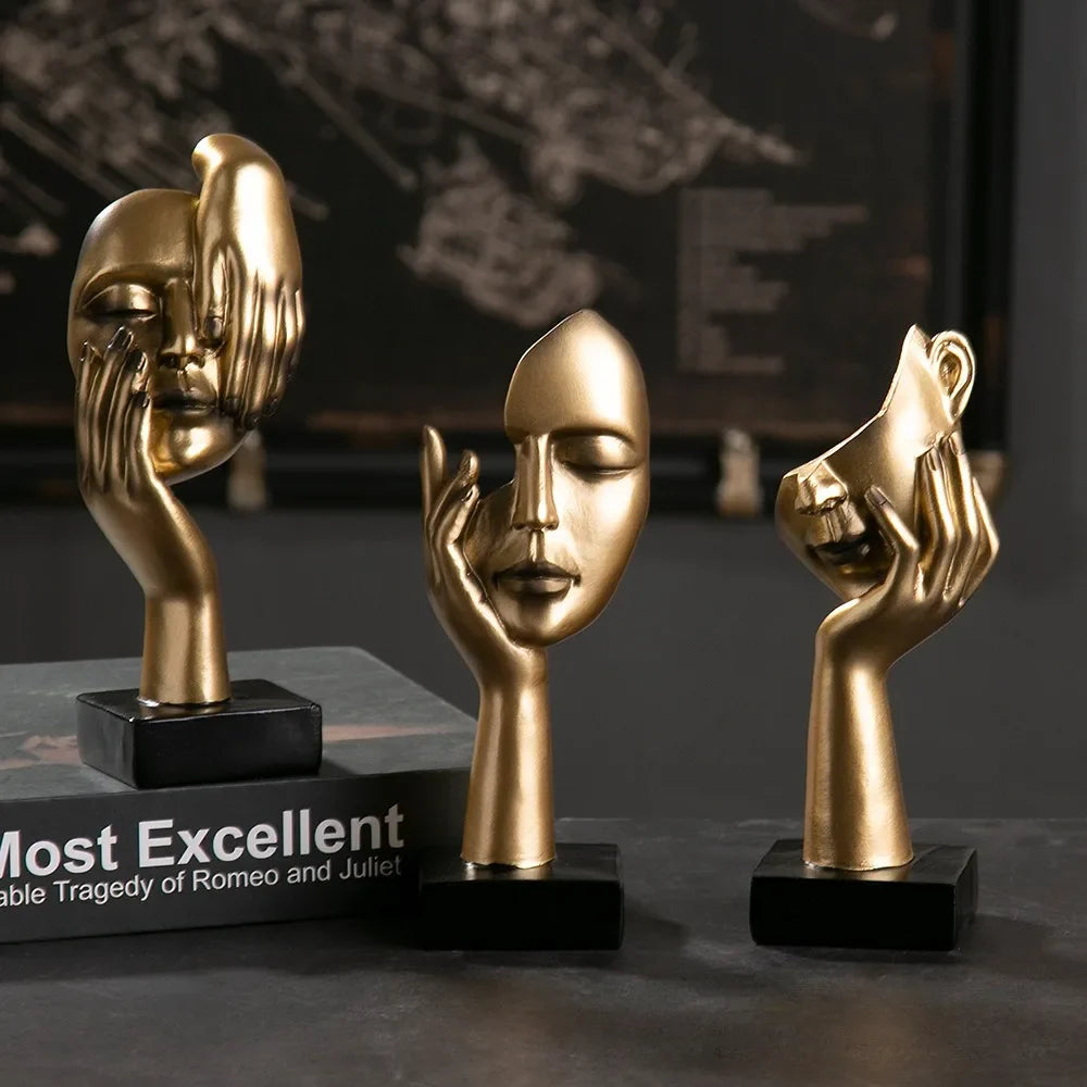Three gold figurines of faces on black bases with a blurred background