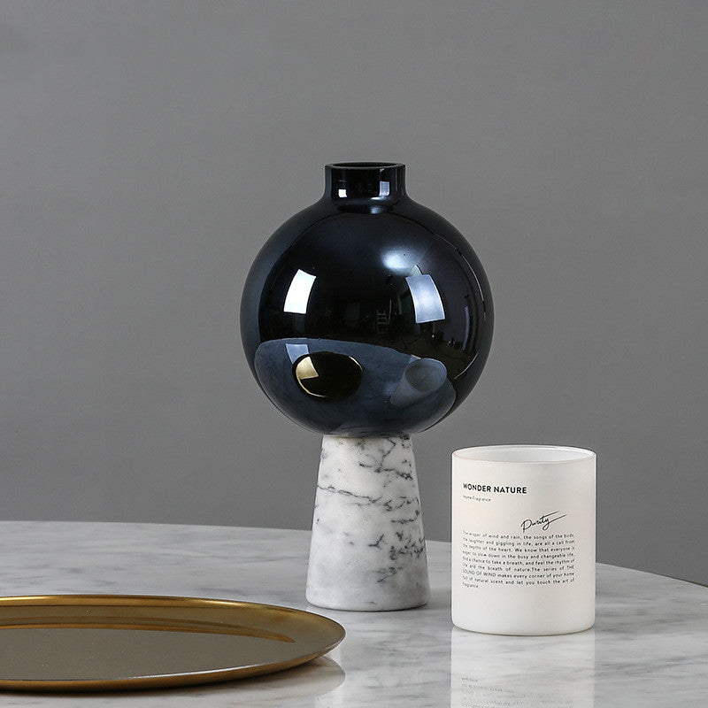Black vase on a marble base with a white candle and gold tray on a gray background