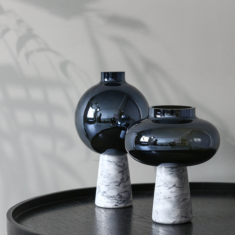 Two black vases with marble bases on a dark surface against a neutral background