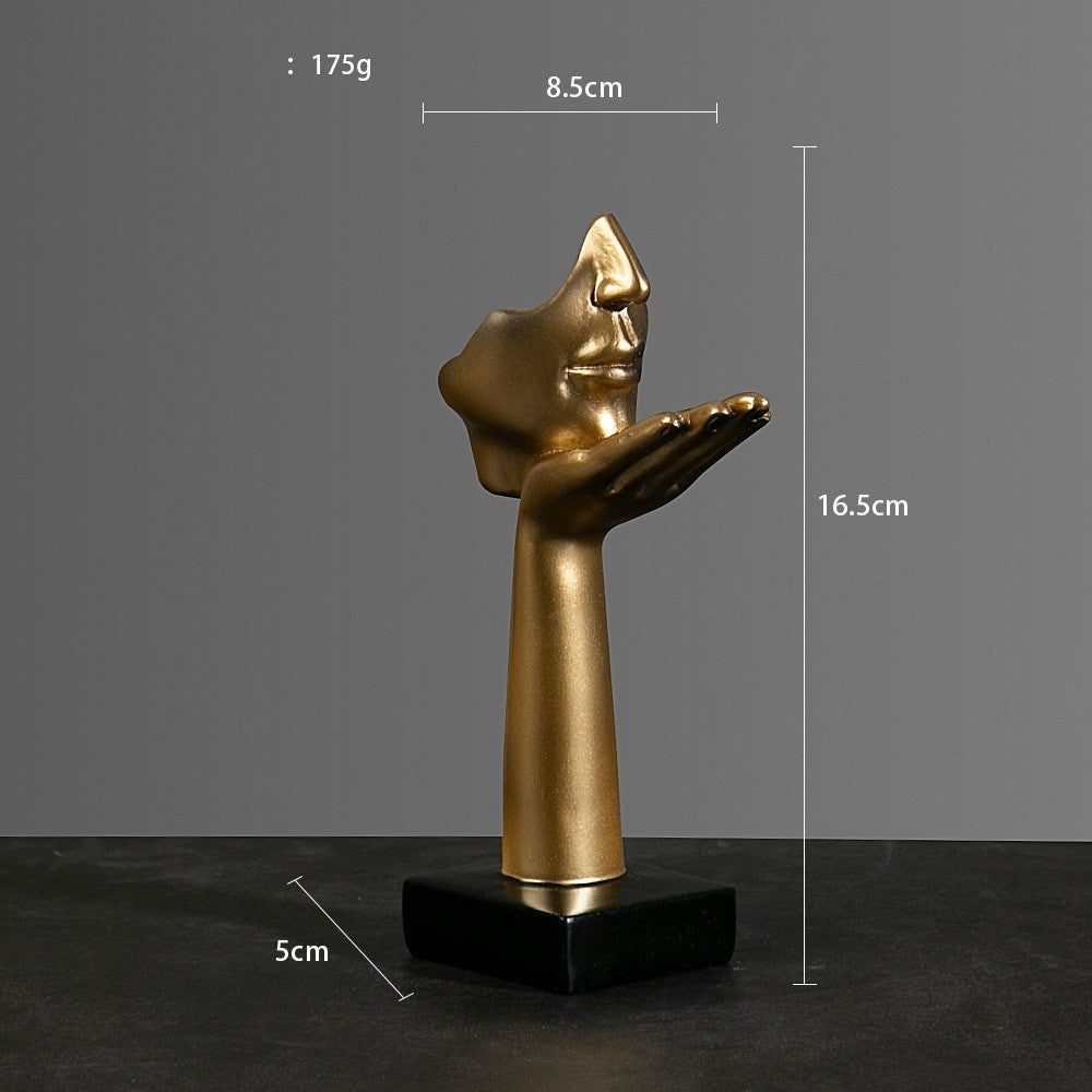 Gold sculpture of a hand with a face on a black base, shown with measurements against a gray background.
