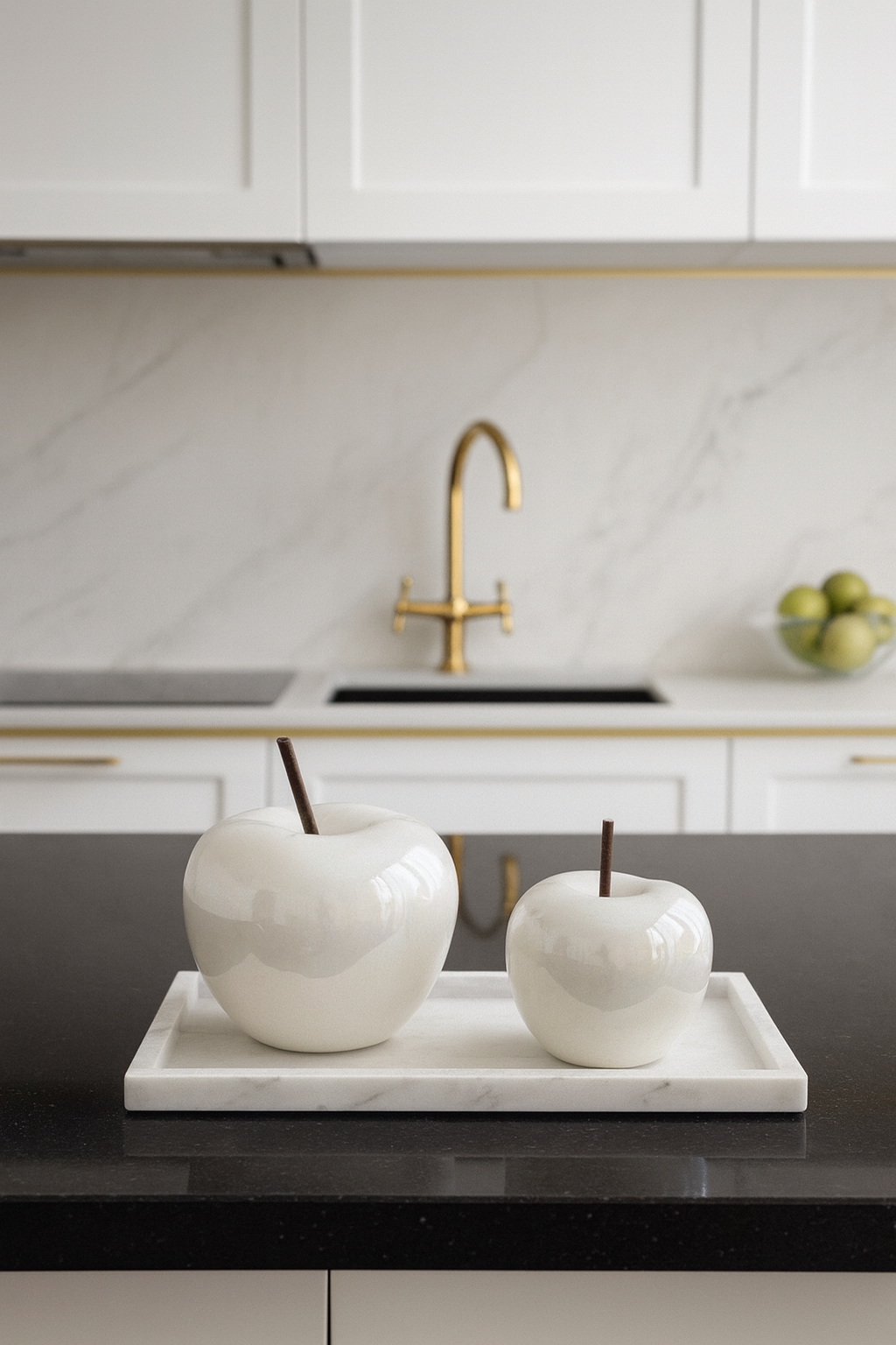 Decorative white apples on a tray in a modern kitchen with a gold faucet.