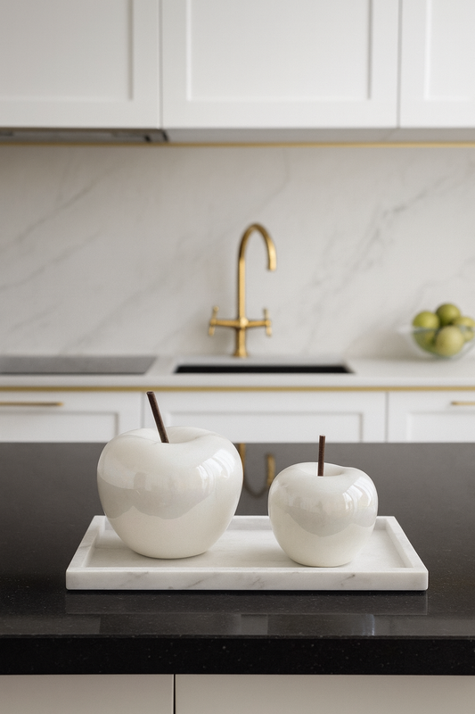 Decorative white apples on a tray in a modern kitchen with a gold faucet.