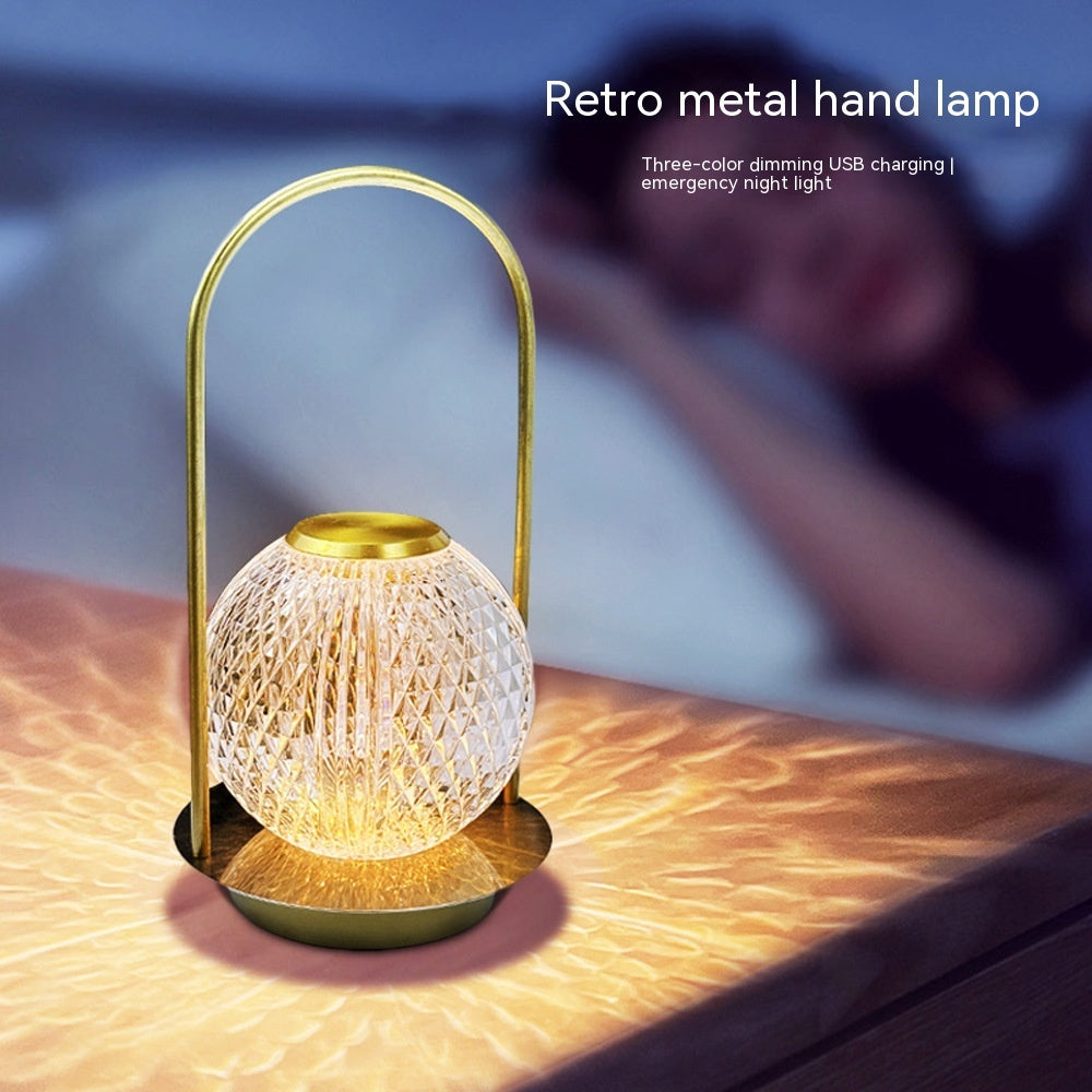 Retro metal hand lamp with gold handle on a wooden surface, glowing softly.