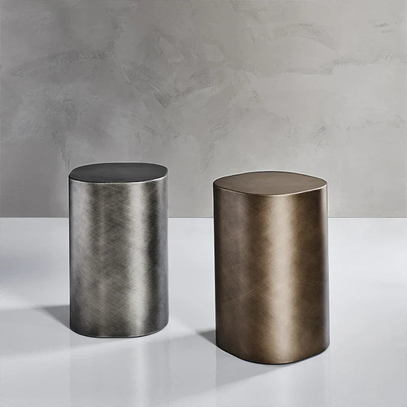 Two cylindrical metal side tables on a white surface with a gray concrete wall background.